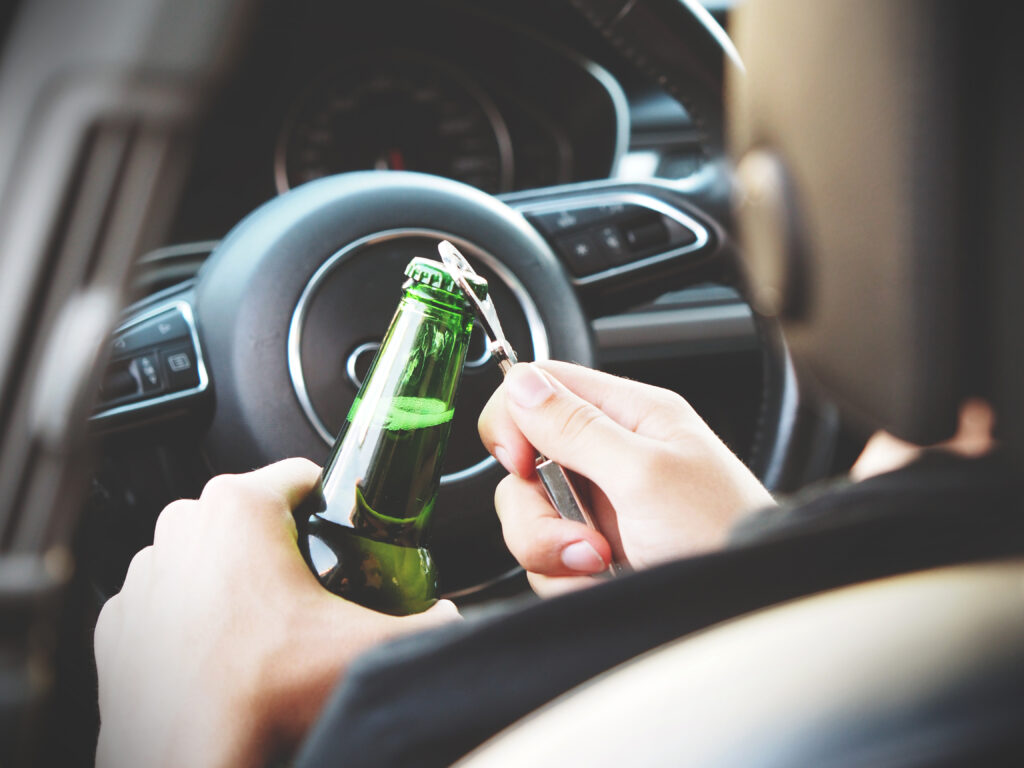Image of a person drinking while driving, likely to get a positive result in a police alcohol test if pulled over or in an accident.